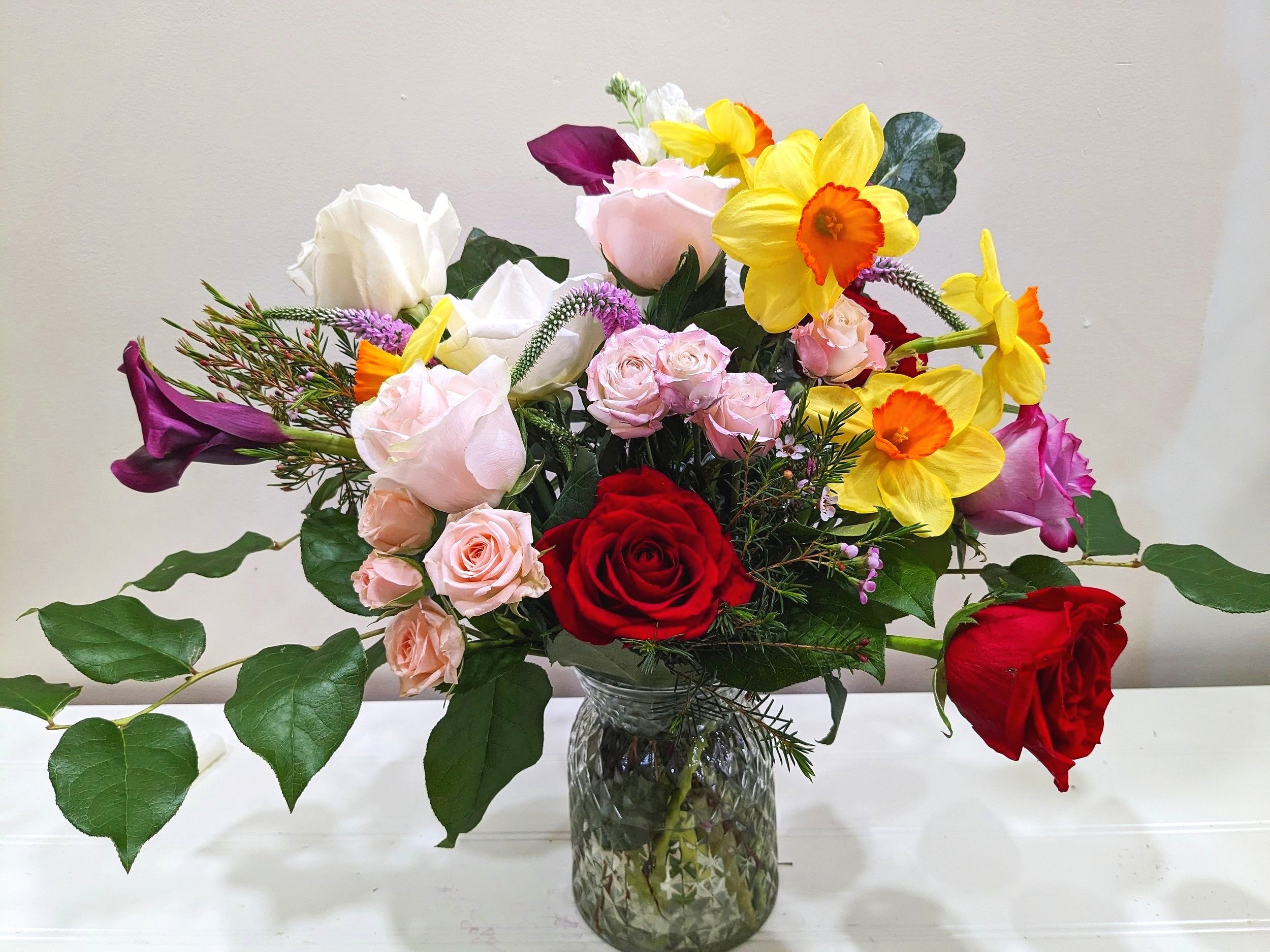"Vertigonia", a large bouquet with red, pink and white roses, yellow and purple flowers in a clear glass vase