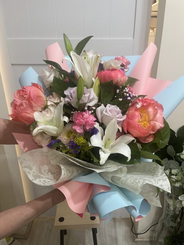 "Colorful", a hand tied bouquet with white lilies, pink flowers and greens in a pastel pink and blue luxe wrap